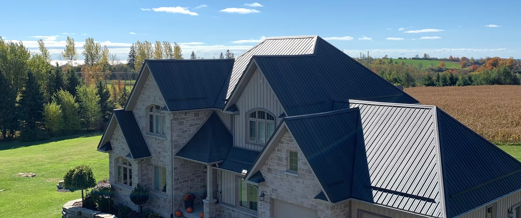 Stone home with dark standing-seam steel roof against a farmland backdrop